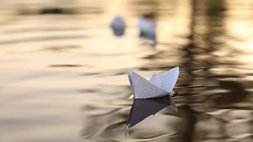 Hand Places Paper Boat on Shimmering Lake