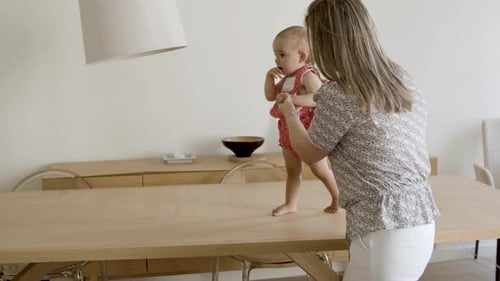 Mother Helping Baby Walk Across Table