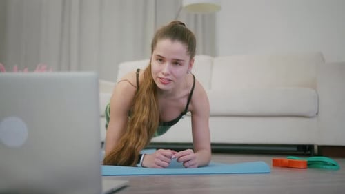 Chica de fitness haciendo ejercicio de tablón mientras usa la computadora portátil para ver un Vídeo tutorial en casa