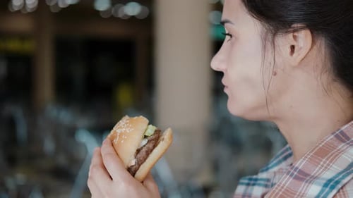 Young Hungry Woman Bites a Burger in a Fast Food Restaurant. The Girl Is Eating a Hamburger.