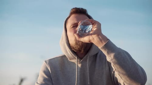 Man Drinking Water Wearing a Hoodie Outdoors