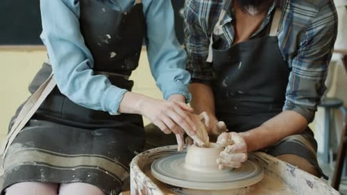 Tilt-up of Girl and Guy Shaping Clay on Pottery Wheel Enjoying Creative Masterclass Together