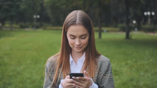 A Young Girl Walks with Her Phone in the Park in the Summer