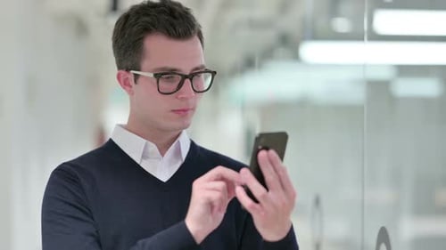 Young Man Celebrating Success on Smartphone in Office