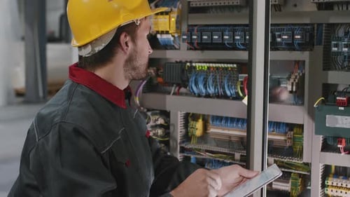 Engineer Inspecting Electrical Control Panel with Tablet