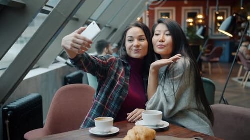 Friends Girls Taking Selfie in Cafe Holding Smartphone Sitting at Table Having Fun Laughing
