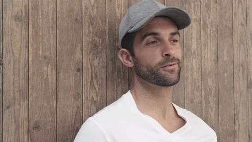 Handsome Man Smiling in Baseball Cap by Wood Wall