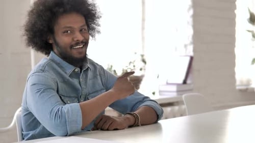 Smiling Man Points at Camera from Desk
