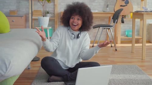 Belle femme afro-américaine avec une coiffure afro assise sur le sol avec un ordinateur portable appris