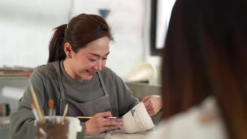 4K Asian woman painting self-made pottery mug with friends at pottery studio.