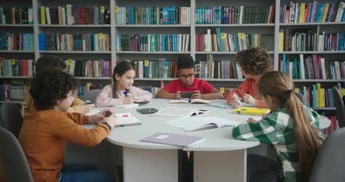 Multinationale Kinder sitzen am runden Tisch in der Schulbibliothek