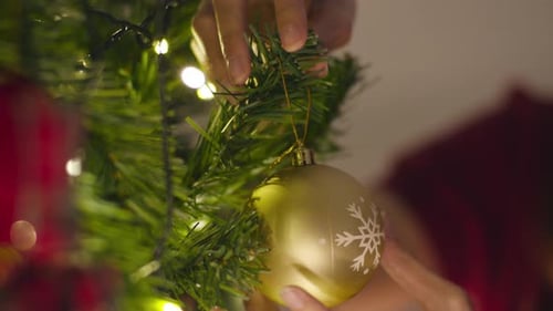 Person Decorating Christmas Tree with Gold Ornament