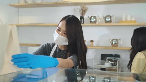 Asian waitress with face protective mask delivering takeaway coffee bags to customers