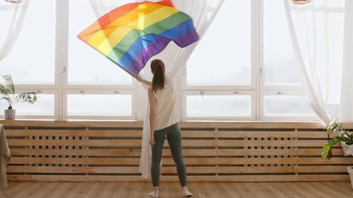 Woman Waving Rainbow Pride Flag Inside Sunny Home