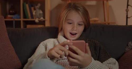 Close Up View of Amazed Little Child Scrolling Phone Screen and Saying Wow While Sitting on Sofa at