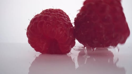 La caméra suit les framboises fraîches tombant à la surface. Ralenti.