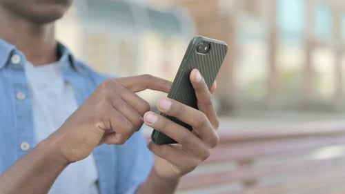 Close Up of Young African Man Using Smartphone While Sitting Outdoor on Bench