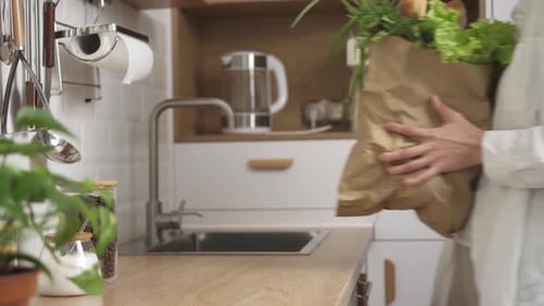 Una mujer joven trae una bolsa de papel con varios productos y la pone sobre la mesa de la cocina