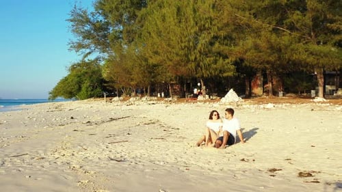Traveling couple exploring white sandy beach of tropical island with pine trees during their vacatio