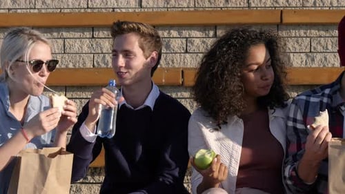 Friends enjoying food together outdoors on a bench