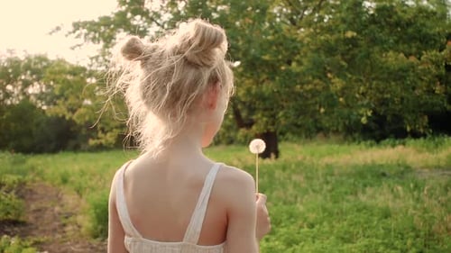 Smiling Girl Holding a Dandelion in Grassy Field