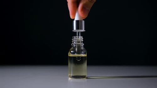Dropper Dispensing Yellow Liquid into Glass Bottle