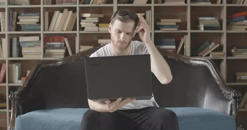 Man Using Laptop on Sofa With Bookshelf