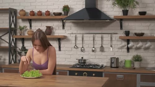 Frau sitzt am Tisch, sieht traurig und gelangweilt von Diät aus und will keinen Salat essen.