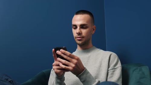 Young Adult Using Smartphone Indoors on Couch