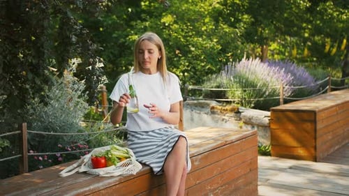 Modelo con verduras y frutas en bolsa de compras de malla reutilizable está sentado en el banco del parque de la ciudad
