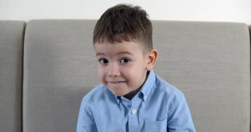 Porträt eines lustigen kleinen Jungen lächelndes Kind, das in die Kamera blickt und zu Hause auf dem Sofa sitzt Süße Vorschule