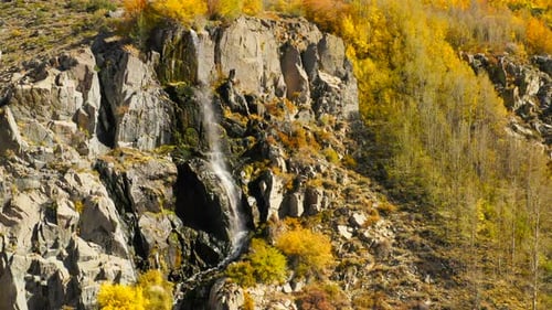 Die Luftaufnahme rund um den Felsen an einem Hang, von dessen einer Seite der Wasserfall herunterfällt.