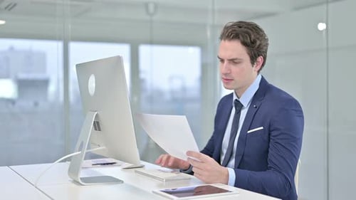 Serious Young Businessman Doing Paperwork in Modern Office