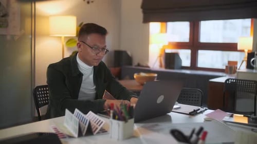 Portrait Of a Bearded Architect Wearing Glasses Sitting in His Office Working Late At Night Looking