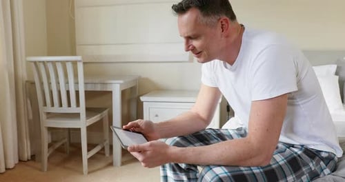 Man Sits On Bed Using Tablet Indoors