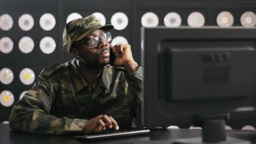 Man in Camo Jacket Talking on Phone at Computer