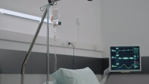 Close Up of IV Drip Bag and Empty Hospital Ward Bed