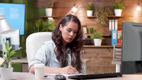 Concentrated Woman Reads an Email and Takes Notes on the Clipboard