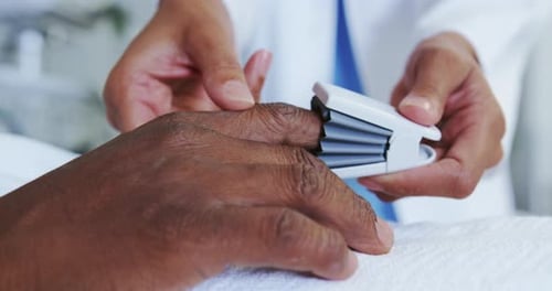 Primer plano de una doctora afroamericana colocando oximetría de pulso en la mano de un paciente masculino en la sala