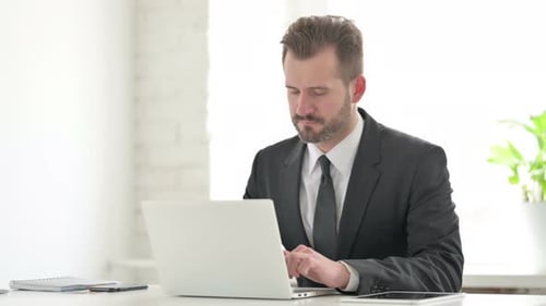 Stressed Man Typing on Laptop in Bright Office
