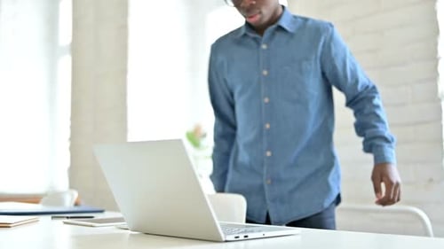 Young African Man Coming Back and Working on Laptop in Office