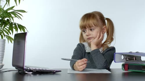 Girl Writes on Paper at Desk with Laptop