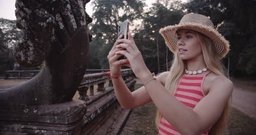 Young Female With Backdrop of Green Trees Pulls Out a Camera Phone to Take Snap