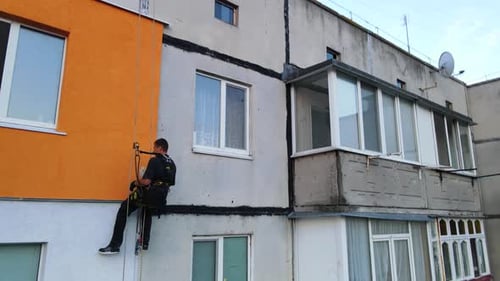 Pintura e decoração de edifícios. Trabalhador em um canteiro de obras de um prédio alto. Perigoso