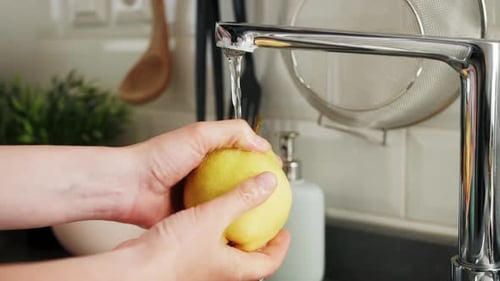 Washing Yellow Pear Under Running Faucet in Kitchen