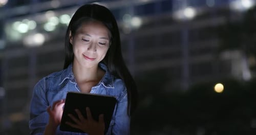 Woman use of tablet computer in city at night