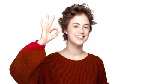 Retrato de uma bela estudante com penteado encaracolado expressando sinal de OK após passar no exame