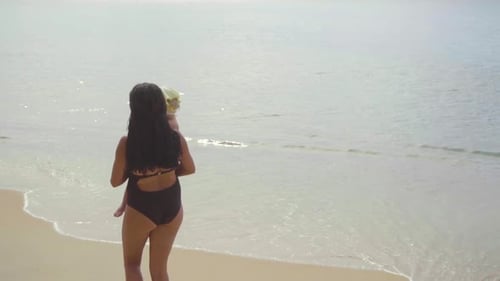 Mom with a Two-year-old Daughter Walking Along the Sandy Beach