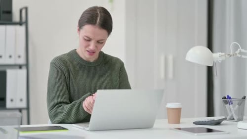 Woman Massaging Wrist While Using Laptop in Office