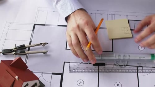 Architect Writing on Sticky Note with Plans